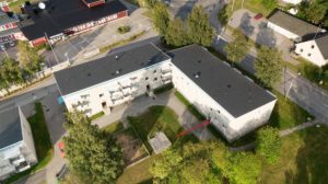En flygvy över ett bostadsområde visar två stora byggnader och en central innergård med gräsytor och träd.