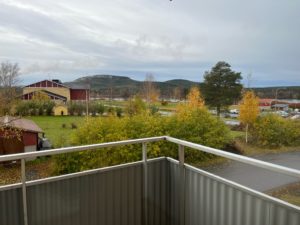 Utsikt från en balkong med utsikt över ett lantligt landskap med en väg, träd i höstlövverk och böljande kullar i fjärran under en molnig himmel. I närheten erbjuder Överkalixbostäder hyreslägenheter för den som vill fördjupa sig i denna fridfulla miljö.