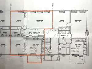 Planritningsskiss som visar flera rum märkta med dimensioner. Ytor inkluderar vardagsrum, sovrum, badrum och hall. Vissa avsnitt är beskrivna i orange. Trappor och diverse inventarier är också synliga med angivna mått.