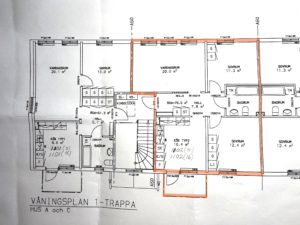 Planlösning för ett flerfamiljshus med flera markerade rum och mått. En central lägenhet är markerad med orange markering, vilket markerar dess rum och planlösning.