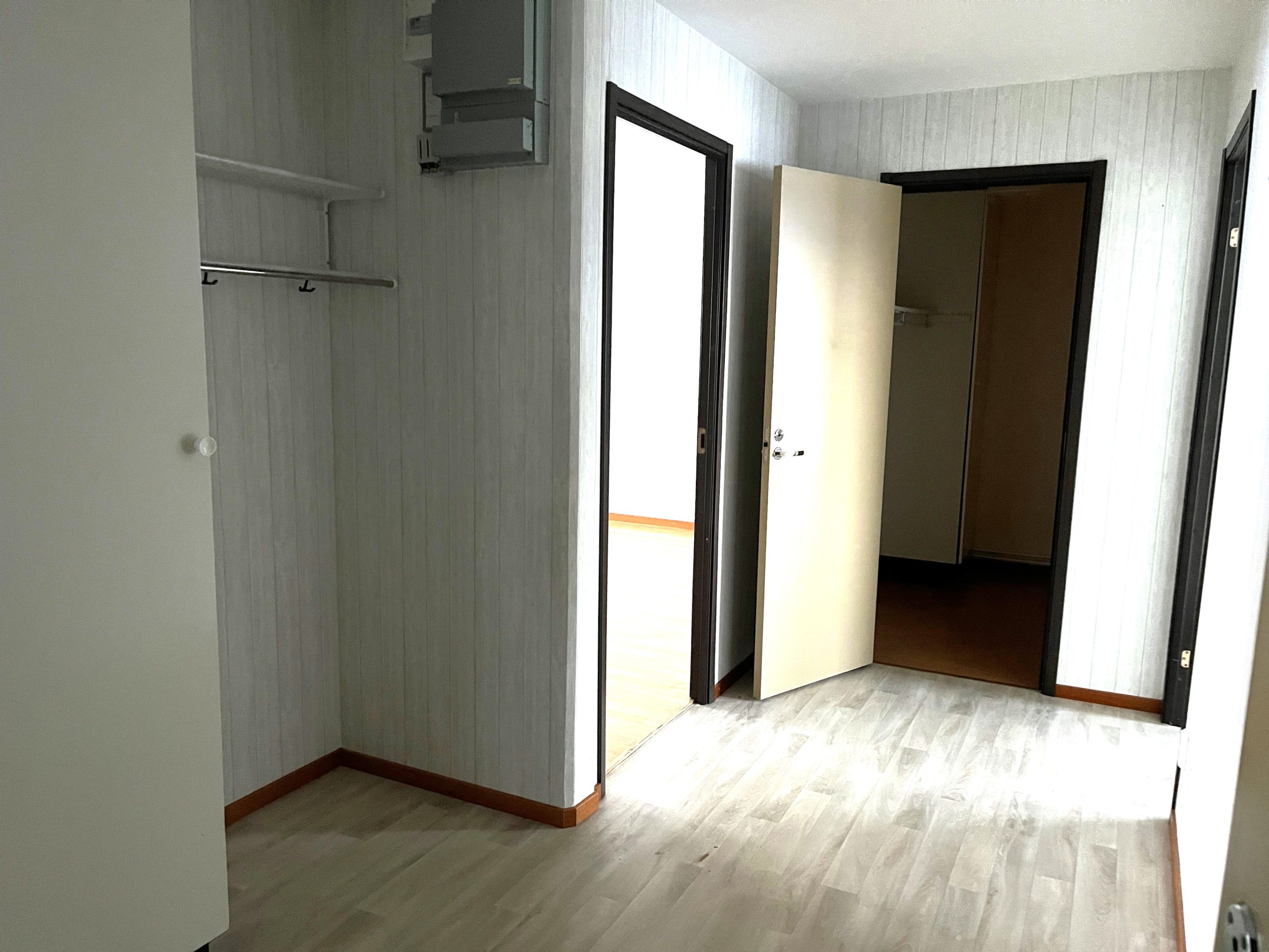 Hall med ljusa väggar och gråfärgat golv. Flera dörröppningar leder till lägenhetens olika rum.