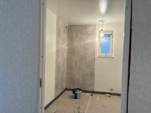 Ett badrum där renovering pågår. Ljusa väggar med en grå våtrumsmatta i vänstra hörnet.