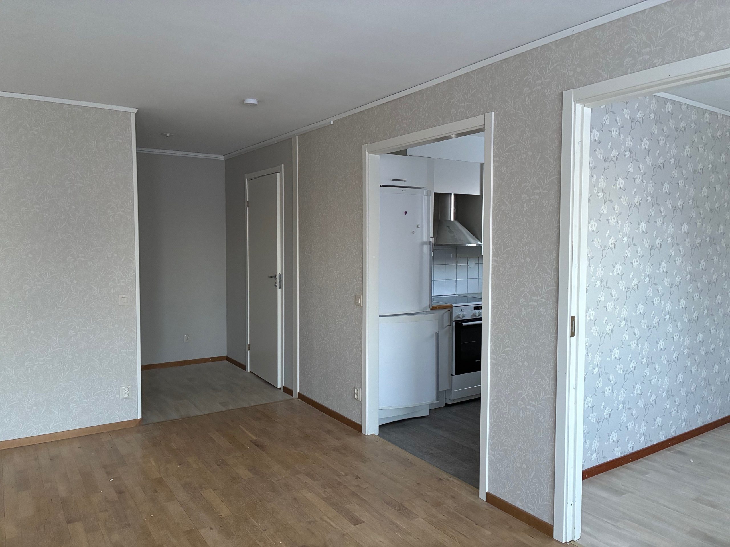 Del av vardagsrum, där man skymtar sovrum, kök samt hall. Genomgående ljusa väggar och träfärgade golv.