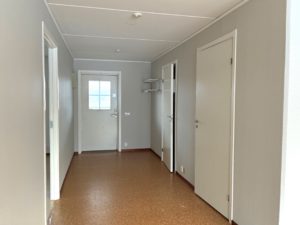 Hall med ljusa väggar och ett brunt golv. Dörrar i korridoren leder till lägenhetens andra rum.
