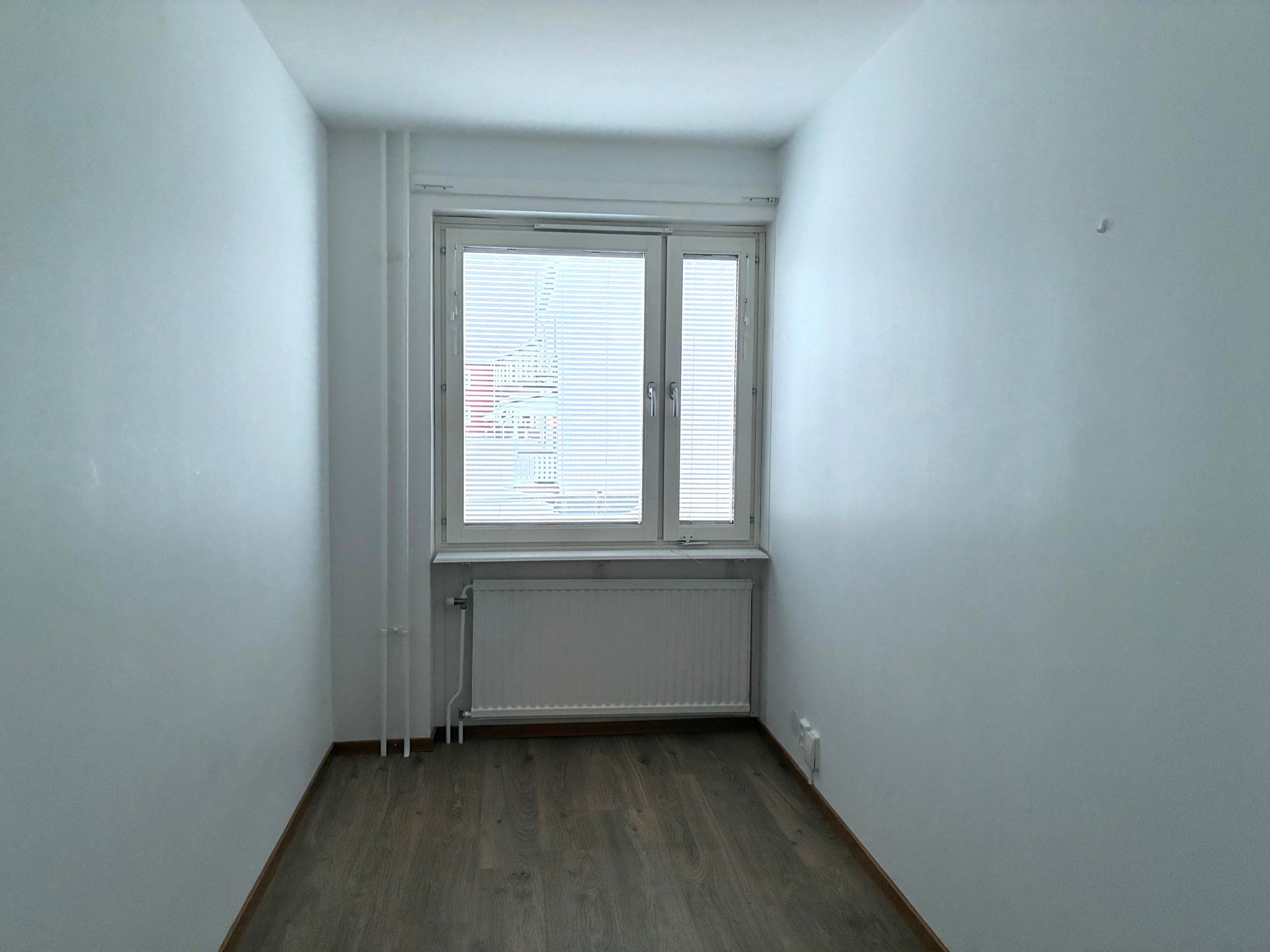 Mindre sovalkov med vita väggar, ett fönster samt träfärgat golv.