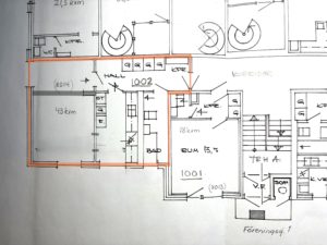 Handritad planlösning för ett flerfamiljshus med flera markerade rum och mått. En central lägenhet är markerad med orange markering, vilket markerar dess rum och planlösning. Handskrivna anteckningar och siffror syns.