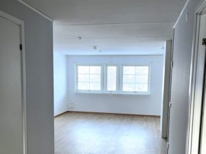 Ljust vardagsrum med flera fönster på den bortre väggen som släpper in ljus.