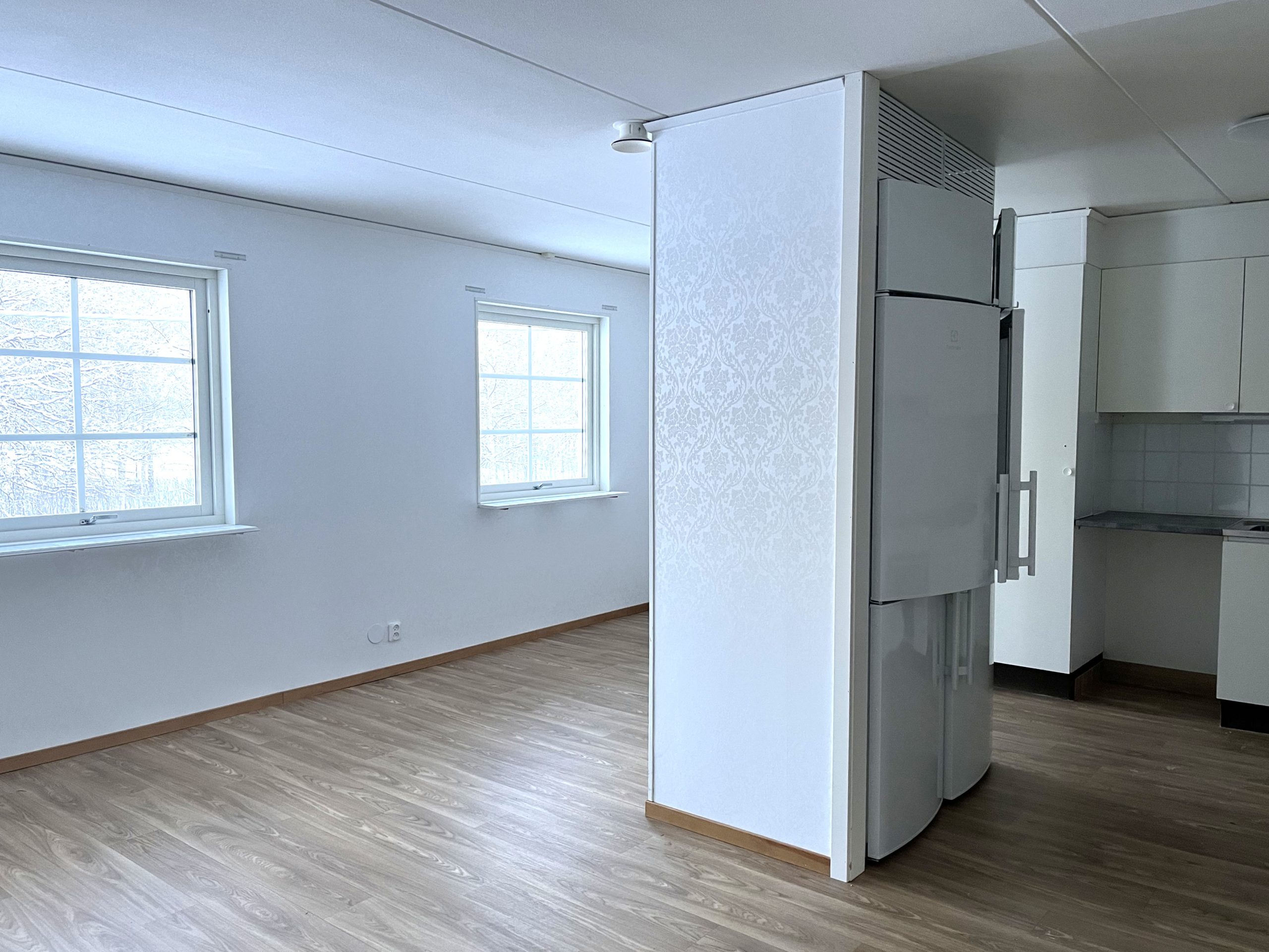 Kök och matplats i en öppen planlösning. Ljusa väggar och ett träfärgat golv. Flera fönster släpper in ljus.