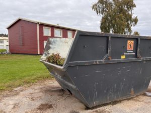 Bilden visar en container märkt med Stiftelsen Överkalixbostäder. I bakgrunden syns ett rött lägenhetshus.